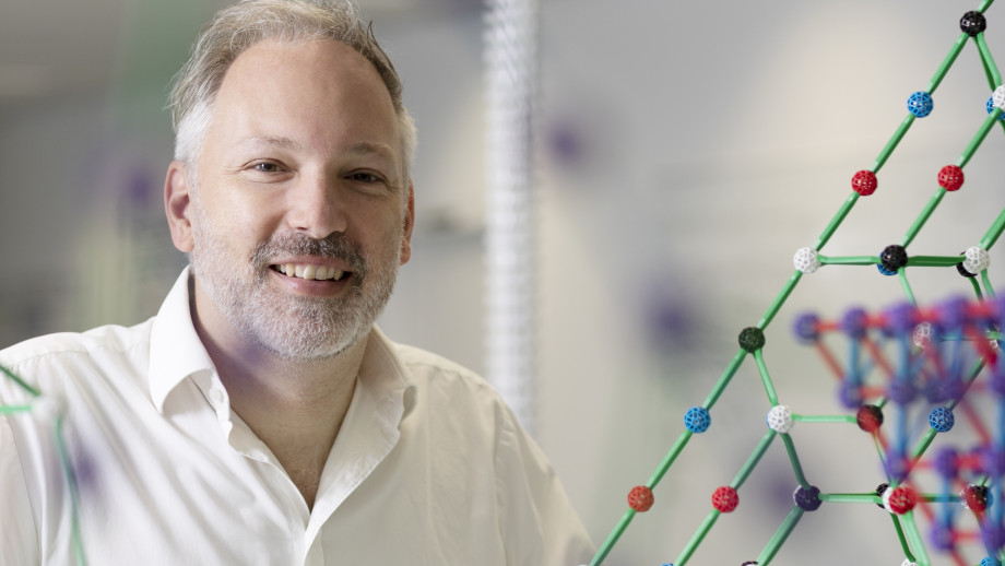 Professor Stephen Bartlett smiles at the camera with models of molecules around him.