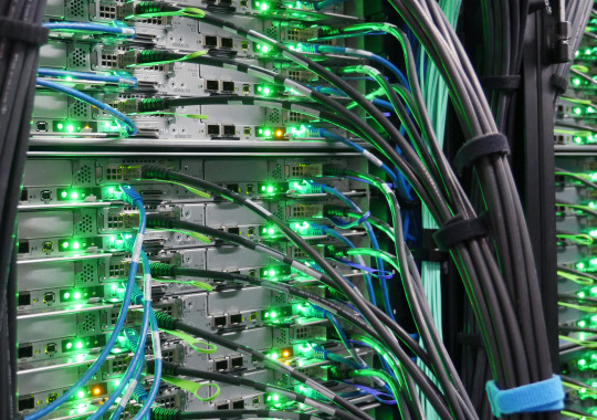 A full rack of a supercomputer with many green flashing lights and cables.