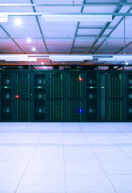 Green lights dotted across the front of a wide bank of dark servers in a darkened room.