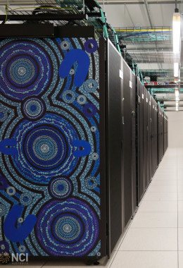Long aisle between two rows of dark computer servers with striking blue artwork on the front face of each row. 	