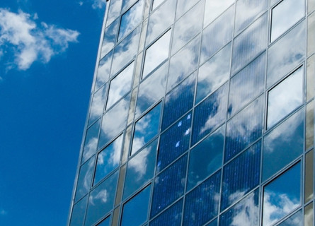 The glass windows of an office building reflecting blue sky and clouds.