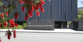 The front facade of NCI seen from the road, partially obscured by red callistemon flowers.