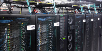 Black mesh cabinets with NCI logos on the front and computer servers, cables and lights visible inside them.