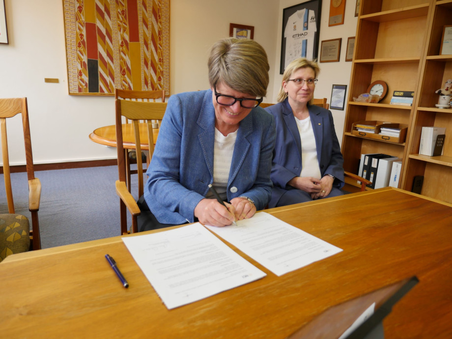 Professor Ann Evans seated on her desk signing the memorandum of understanding.