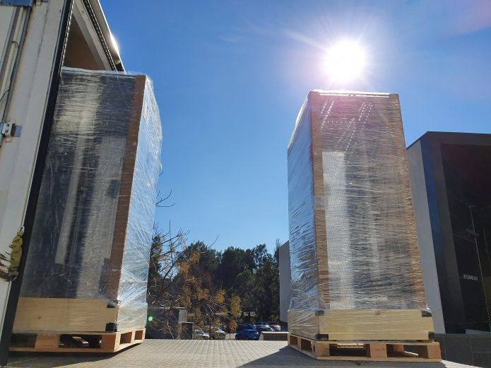 Two tall pallets wrapped in clear plastic sit on the loading bay of a delivery truck.