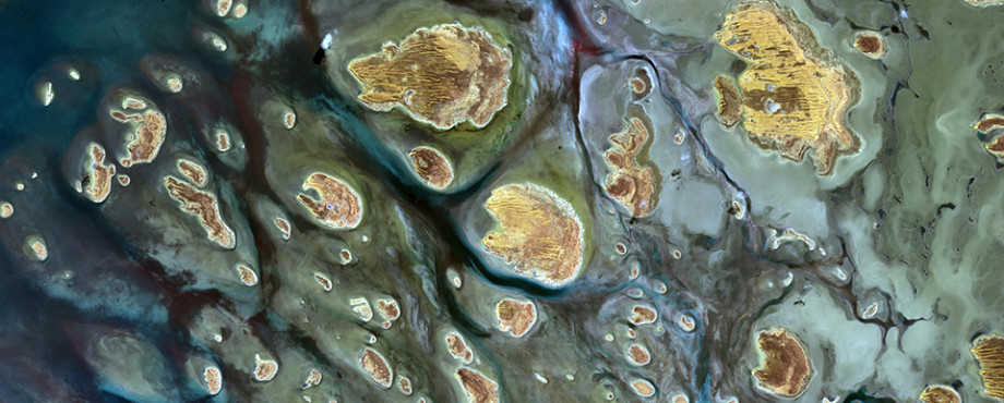 A group of sandy islands seen from above with dark green and blue water flowing around them.