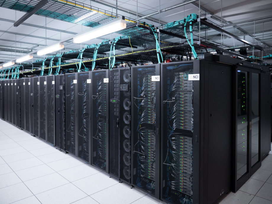 A row of black mesh cabinets with silver computer servers, cables and lights showing through.