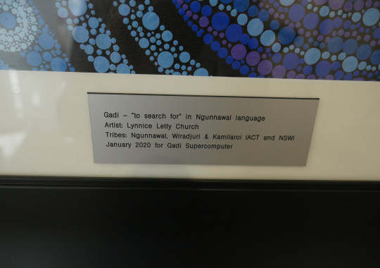 A silver name plate stating the name (Gadi) and artist (Lynnice Letty Church) of the blue artwork visible above it.