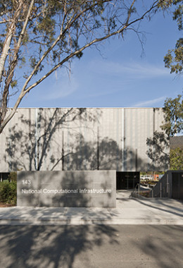 The front facade of the NCI building serving as a backdrop to shadows of tall trees standing in front of the building.