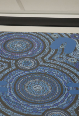 Top half of an intricate blue and purple painting showing dots and rings framed with a white border and black frame, as seen from below.