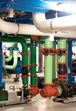 Light green, dark green, blue and white pipes connected to orange pumps in a large room.