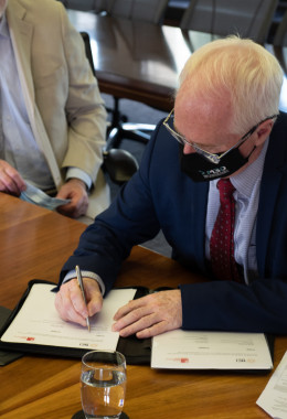 A man in a dark blue suit signs an important document.