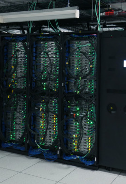 Front-on view of a pod of server racks, with blue cables and green flashing lights.