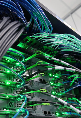 Close-up picture of a range of computer cables plugged into servers with bright green flashing lights.