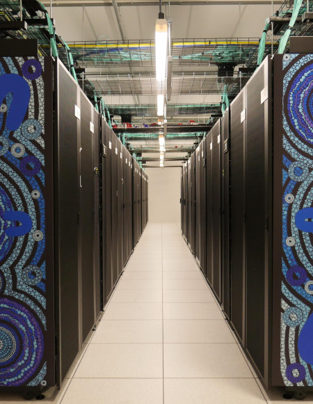 Long aisle between two rows of dark computer servers with striking blue artwork on the front face of each row.