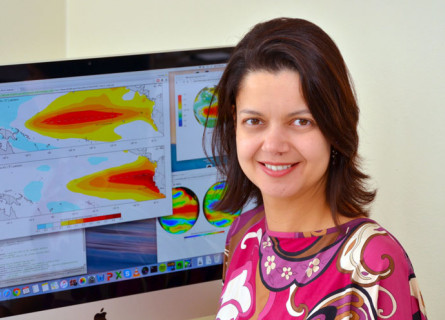 Andrea Taschetto sits in front of a computer showing brightly coloured world maps.
