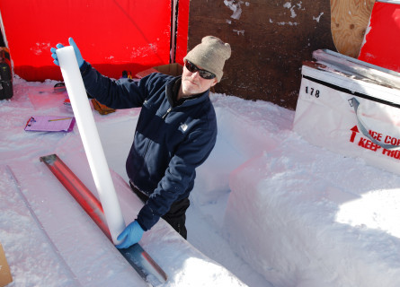Andrew Smith stands in a hollow in the ice while holding a long cylindrical ice core.