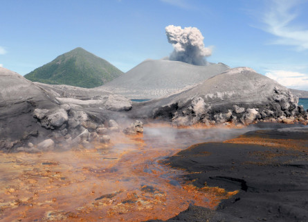 A green pointed mountain in the background, a cone shaped volcano with a cloud of smoke coming out of it in front, and a steamy orange lake in the foreground.