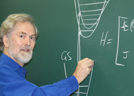 Professor Jeffrey Reimers stands at a blackboard writing equations.