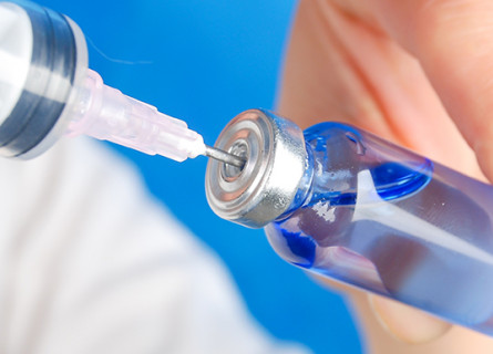 A syringe sucking liquid out from a blue glass vial.