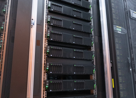 A tall rack comprising around a dozen horizontal black computer servers stacked on top of each other.