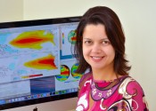 Andrea Taschetto sits in front of a computer showing brightly coloured world maps.