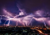 Ten bolts of lightning hitting a city in the distance, with purple illuminated clouds.