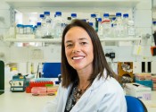 Carola Vinuesa sits smiling at the camera in front of a lab bench filled with jars and other scientific equipment.