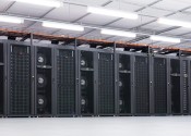The NCI supercomputer Raijin, columns of black computer servers separated by stacks of in-row fans, in a big white room.