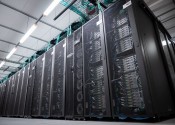 Black mesh cabinets with silver computer servers, cables and lights visible inside them.