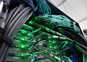 Close-up picture of a range of computer cables plugged into servers with bright green flashing lights.