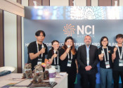 Seven people standing in front of NCI logo in a conference booth, six holding small koalas.