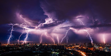 Ten bolts of lightning hitting a city in the distance, with purple illuminated clouds.
